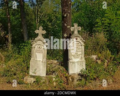 Two old worn stone gravetombs in between trees and shrubs in the Transylvanian countryside, Romania Stock Photo