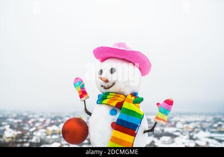 Snowwoman with Christmas toy. Snowman holds new year ball. Snow man in pink hat. Christmas. Funny snowman. Merry Christmas and Happy new year Stock Photo