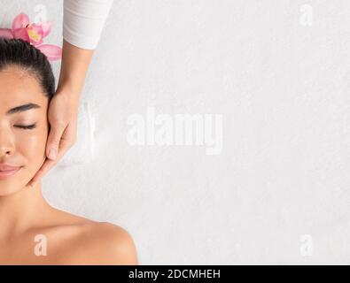 Beauty And Spa. Relaxed asian lady enjoying facial massage at wellness center Stock Photo