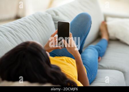 Unrecognizable black woman using cellphone on comfy sofa at home, mockup for mobile app design on screen Stock Photo