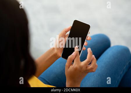 Unrecognizable black woman using cellphone with empty screen indoors, mockup for mobile app or website design Stock Photo
