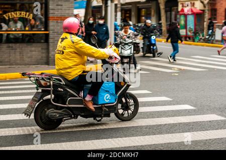 A Meituan delivery guy on a scooter with an Eleme delivery bag at the intersection of Jiaozhou and Wuding Roads in Shanghai’s Jing’an District. Stock Photo