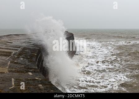 A wave breaking over the seawall known as The Cobb at Lyme Regis on the Jurassic Coast in Dorset on a foggy winters day Stock Photo