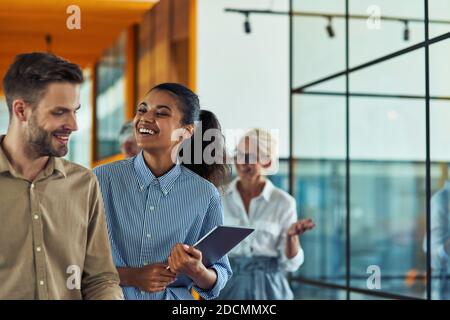 Two young cheerful diverse colleagues talking after business meeting while standing in the modern office or coworking space Stock Photo