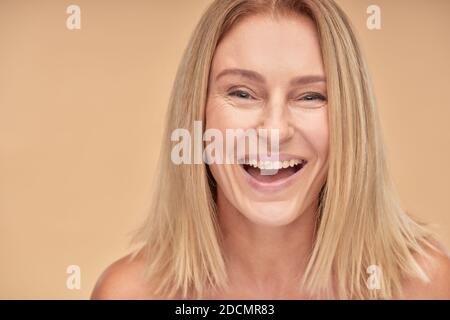 Portrait of attractive happy mature lady smiling at camera while posing over beige background in studio Stock Photo
