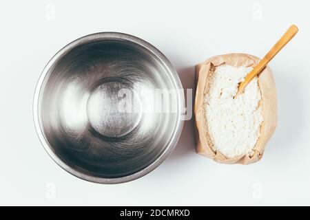 Empty metal bowl and pack of flour with wooden spoon, minimal cooking flat lay composition on white background. Stock Photo