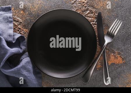 Empty black ceramic plate and cutlery on the table, top view. Food background Stock Photo