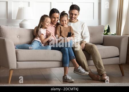 Married couple with daughters resting on couch using smartphone Stock Photo
