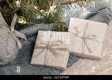 Close up two DIY gift boxes, fir branches, Xmas lights, knitted Xmas ball on grey plaid. Warm homely cozy winter Danish hygge concept. Hugge atmospher Stock Photo