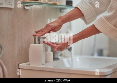 Woman hands using soap dispenser standing on basin at bathroom. Beauty, skincare and cosmetology concept Stock Photo
