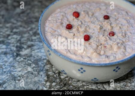 Fresh yogurt with cereals, sliced fruits, banana, apple, decorated with small strawberry from the woodland. Prepared Swiss bircher muesli. Copy space. Stock Photo