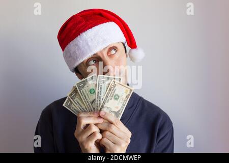 Young man with Santa hat holding dollar bills with dreamy look over white background. Person looking up with cash in hands. New year resolution Stock Photo