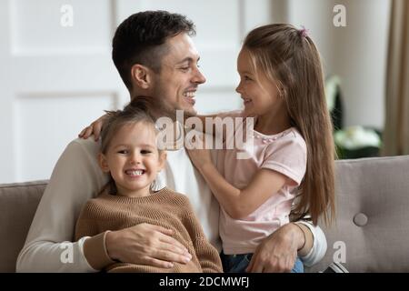 Father sitting on couch hugging two little daughters Stock Photo