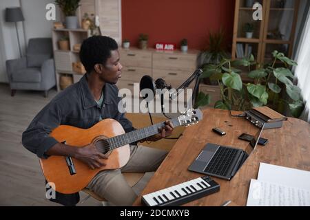 High angle portrait of young African-American man playing guitar and singing to microphone in home recording studio, copy space Stock Photo