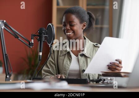 Portrait of smiling African-American woman singing to microphone while recording music in home studio, copy space Stock Photo