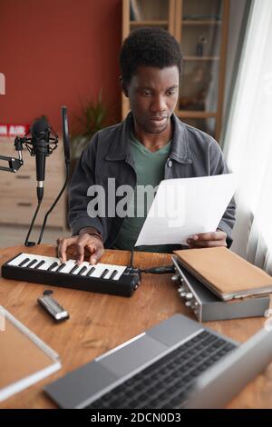 Vertical portrait of young African-American musician composing music in home recording studio Stock Photo