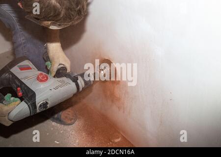 a worker with a drill with a nozzle drills a hole for an electrical outlet. Stock Photo