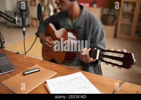 Cropped portrait of talented African-American man singing to microphone and playing guitar while recording music in studio, copy space Stock Photo