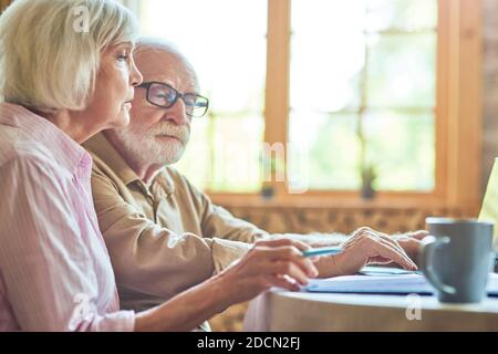 Side view of senior couple using laptop while checking bills together at home. Copy space. Family and household concept Stock Photo