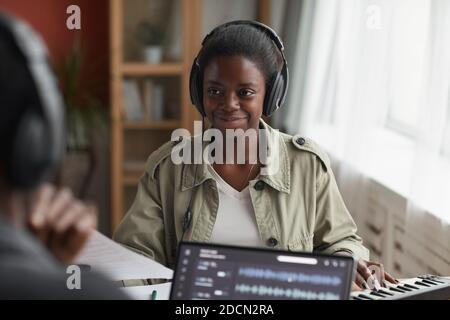 Portrait of smiling African-American woman wearing headphones while composing music in recording studio Stock Photo