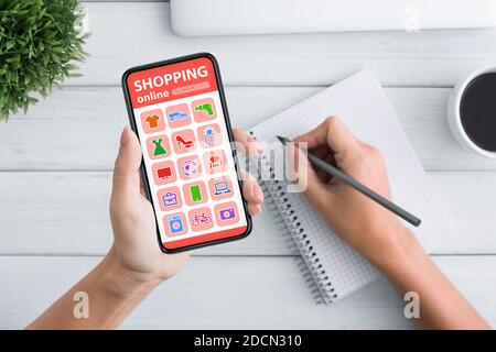 Woman Shopping Online On Mobile Phone And Taking Notes, Closeup Stock Photo