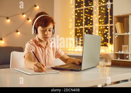 Serious schoolboy staying home on winter holidays and focusing on studies using his laptop Stock Photo