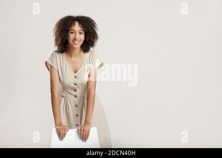 Portrait of cheerful curly african american young woman leaning on chair looking at camera and smiling Stock Photo