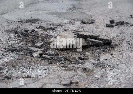 A rough broken roadway. Pieces of broken asphalt lie in a hole in the road. The road is patched and cracked. Stock Photo