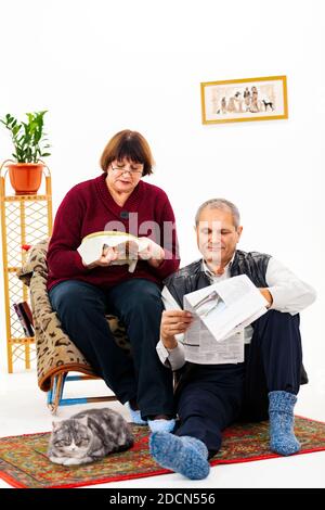 Caucasian grandmother is embroidering, grandfather is reading a newspaper together, a cat is lying nearby Stock Photo