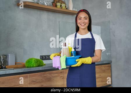 https://l450v.alamy.com/450v/2dcn5rm/happy-young-woman-cleaning-lady-smiling-at-camera-holding-container-full-of-cleaning-supplies-and-equipment-while-standing-in-the-modern-kitchen-housework-and-housekeeping-cleaning-service-concept-2dcn5rm.jpg