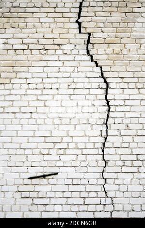 a large long and wide crack in a white brick wall Stock Photo