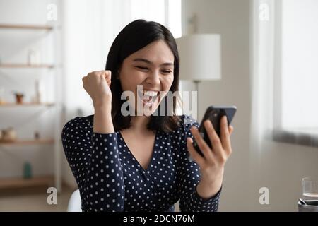 Close up overjoyed Asian woman reading good news, celebrating success Stock Photo