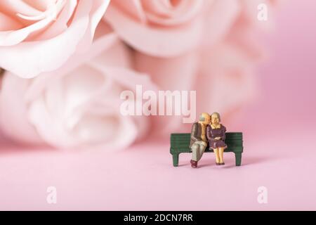A closeup shot of old couple figurines sitting on a bench on rose background