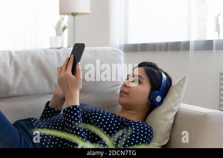 Relaxed Asian woman wearing headphones using smartphone, watching video Stock Photo