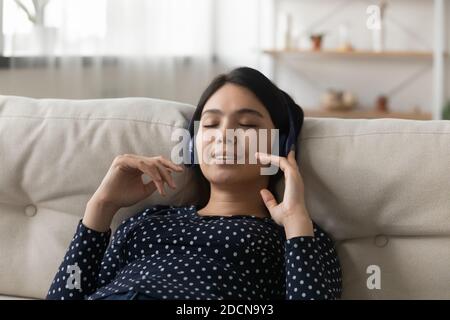 Close up peaceful Asian young woman wearing headphones enjoying music Stock Photo