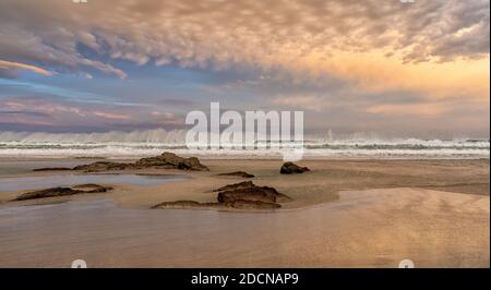 A sunrise on a beautiful empty beach with waves crashing and rocks in the sand Stock Photo