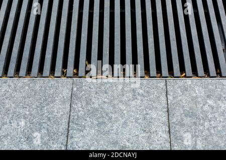 grating of the drainage storm system on the pedestrian park sidewalk made of gray stone granite tiles and an iron storm cover on the floor, nobody. Stock Photo