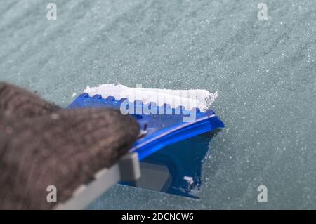 a blue plastic scraper hold by a hand in black glove at a windshield Stock Photo