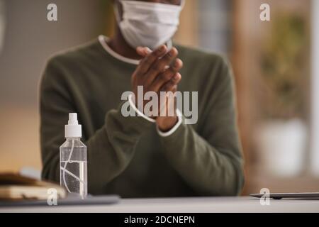 Cropped portrait of African-American man sanitizing hands at workplace with focus on spray bottle in foreground, copy space Stock Photo