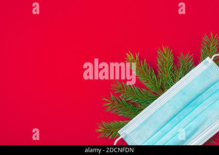 Christmas background during pandemic of Covid 19 made from face mask and fir tree on red background. flat lay. top view with copy space Stock Photo