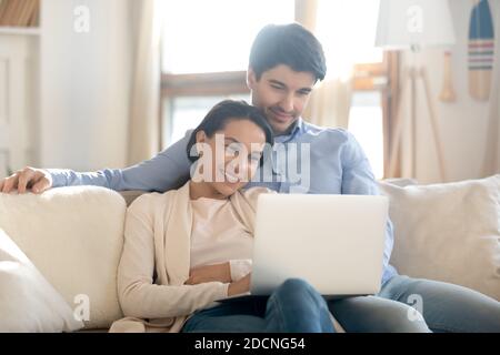 Loving young couple cuddling on couch watching film on laptop Stock Photo