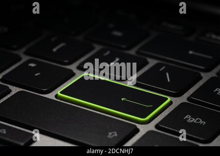 Green enter key on laptop keyboard in the dark. Selective focus. Stock Photo