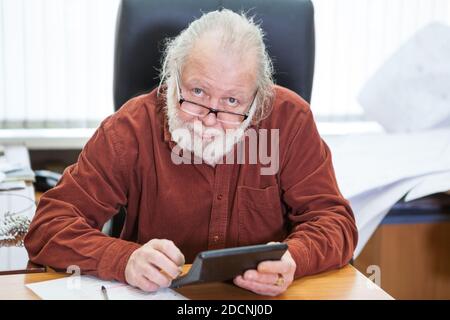 Portrait of European man with a beard holding a calculator in his hands, office room Stock Photo