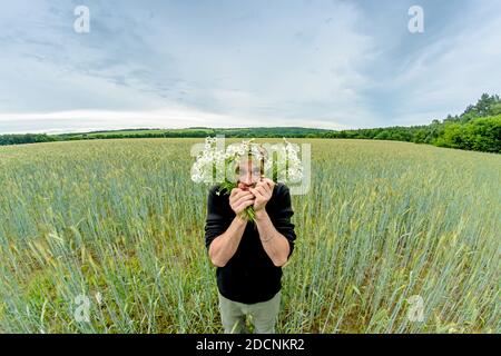 A man with a bouquet of daisies field stands in the middle of a wheat field. Stock Photo