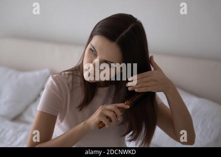 Anxious millennial female brushing long hair troubled with unhealthy look Stock Photo