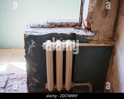 Old white battery on a dilapidated wall in an apartment Stock Photo