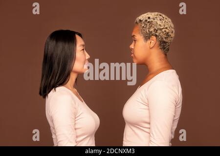 Side view of two young intercultural women in white pullovers in front of camera Stock Photo