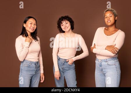Young joyful women in white pullovers and blue jeans standing in front of camera Stock Photo