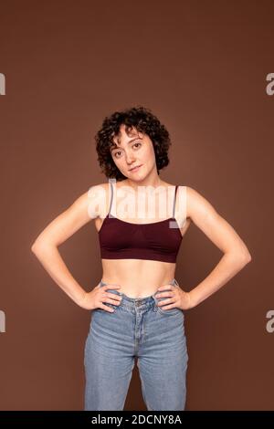 Young gorgeous brunette woman with short curly hair keeping her hands on waist Stock Photo