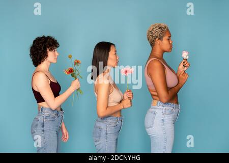 Side view of three young women in tanktops and blue jeans holding fresh flowers Stock Photo